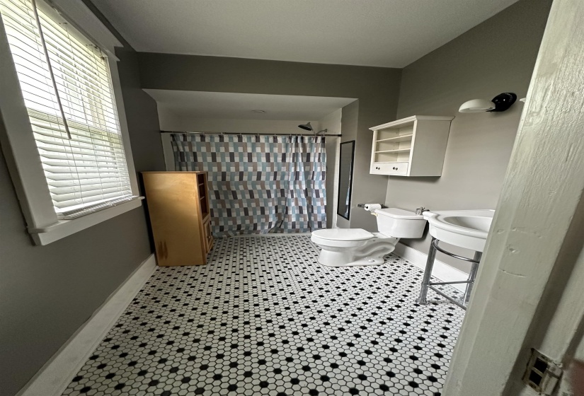 Bathroom featuring white and black hexagonal tile flooring, a pedestal sink, and a window with blinds