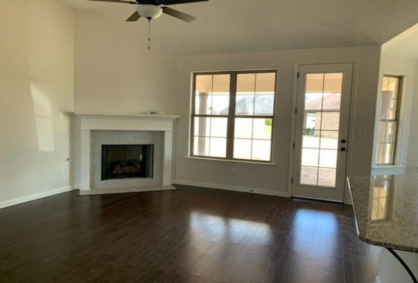 Spacious living area featuring a fireplace with stone surround, high ceilings, dark wood-finish flooring, and a ceiling fan