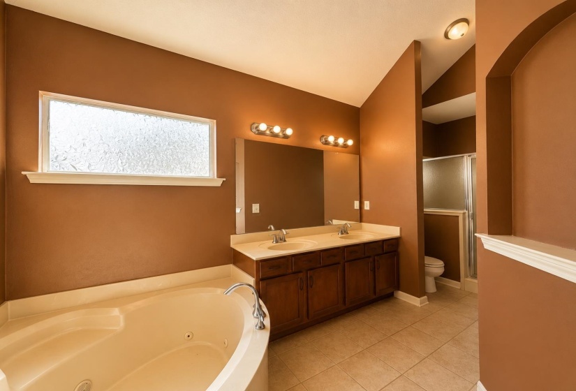 Bathroom featuring a corner soaking tub, textured privacy window, and tile flooring