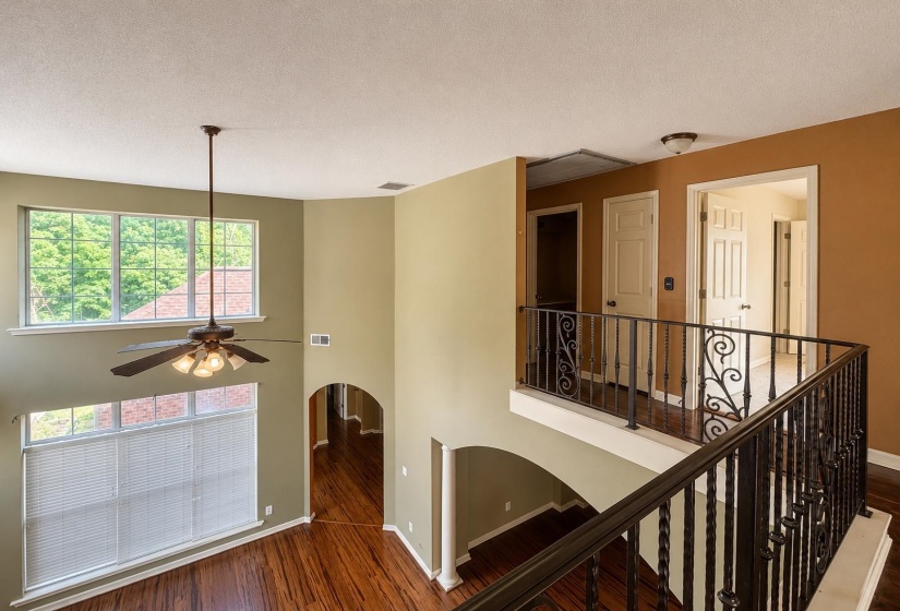 Two-story interior featuring a wrought iron railing, wood-finish flooring, and arched doorways