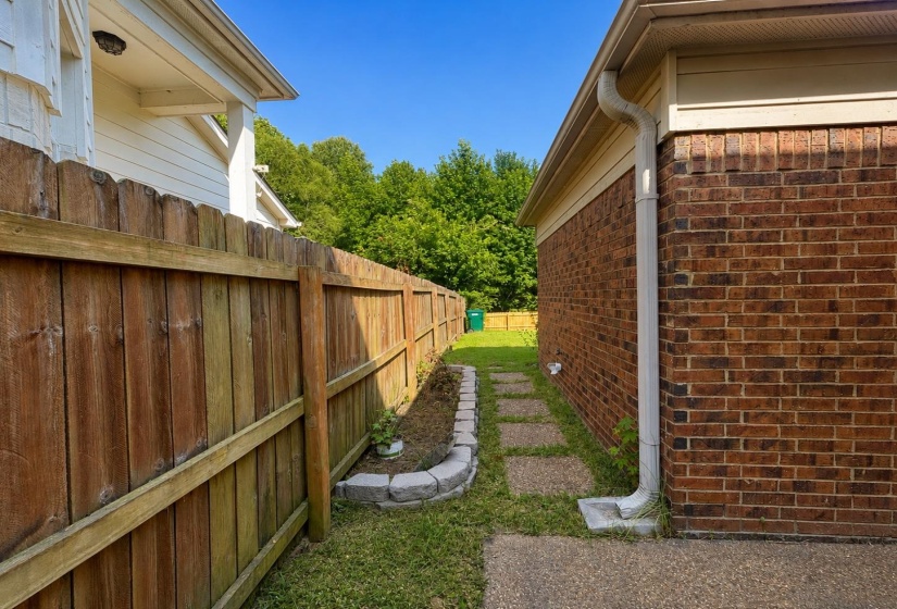 Side yard from courtyard featuring a wood privacy fence, brick exterior, stone paver pathway, and a raised garden bed with stone edging