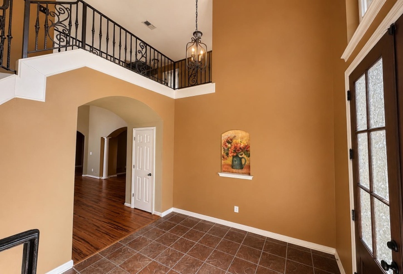 Entryway featuring high ceilings, a hanging chandelier, decorative wrought iron railing, arched doorways, and tile flooring