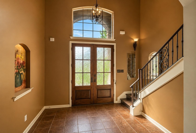 Two-story foyer featuring double wood-panel doors with frosted glass, transom window, and a wrought iron staircase