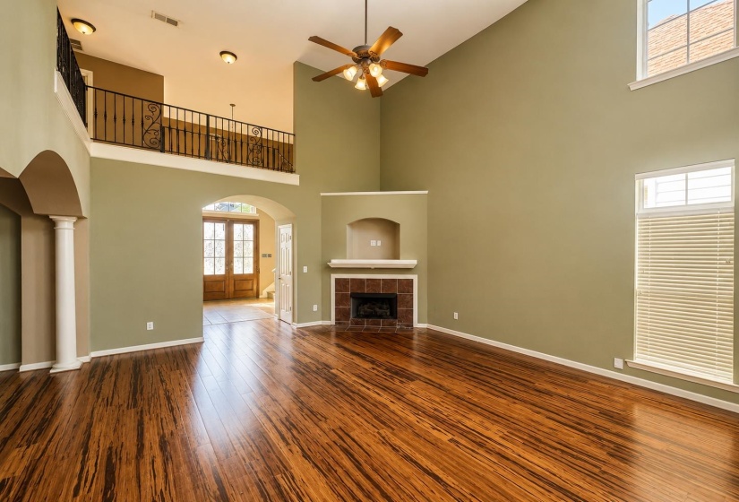 Two-story living area featuring high ceilings, wood-finish flooring, and a fireplace with a tile surround and mantel