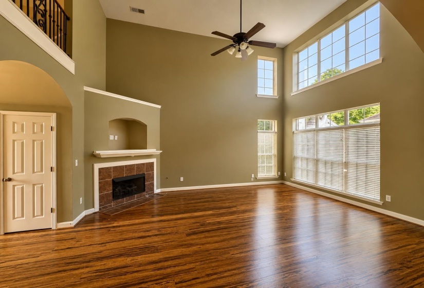 Spacious living area featuring high ceilings, wood-finish flooring, a ceiling fan, and extensive windows with blinds