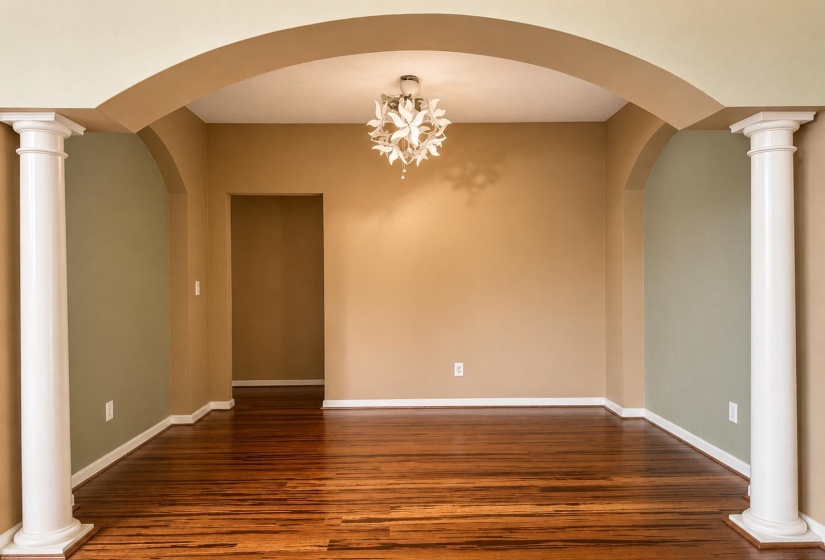 Spacious dining room featuring wood-finish flooring, decorative archways, and architectural columns