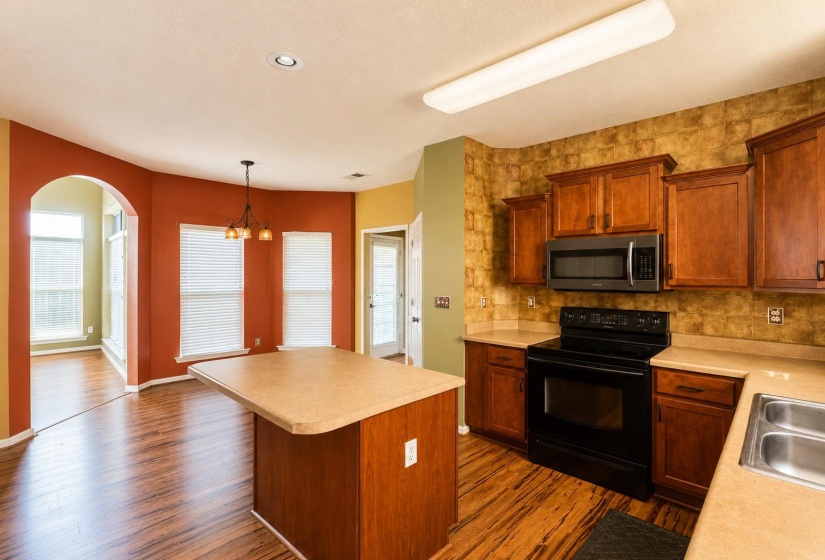 Kitchen featuring wood-finish flooring, a central island, wood cabinetry, stainless steel microwave, and a double basin sink