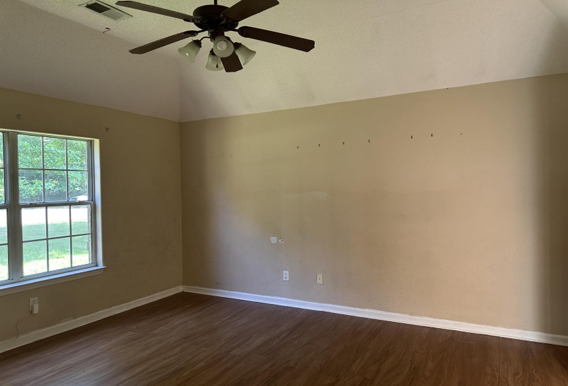 Vaulted ceiling room featuring wood-finish flooring, a ceiling fan with integrated lighting, and a double-hung window