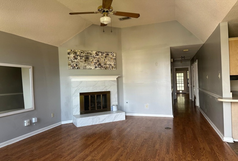 Living area with vaulted ceiling, wood-finish flooring, a white marble-look fireplace surround, and a ceiling fan
