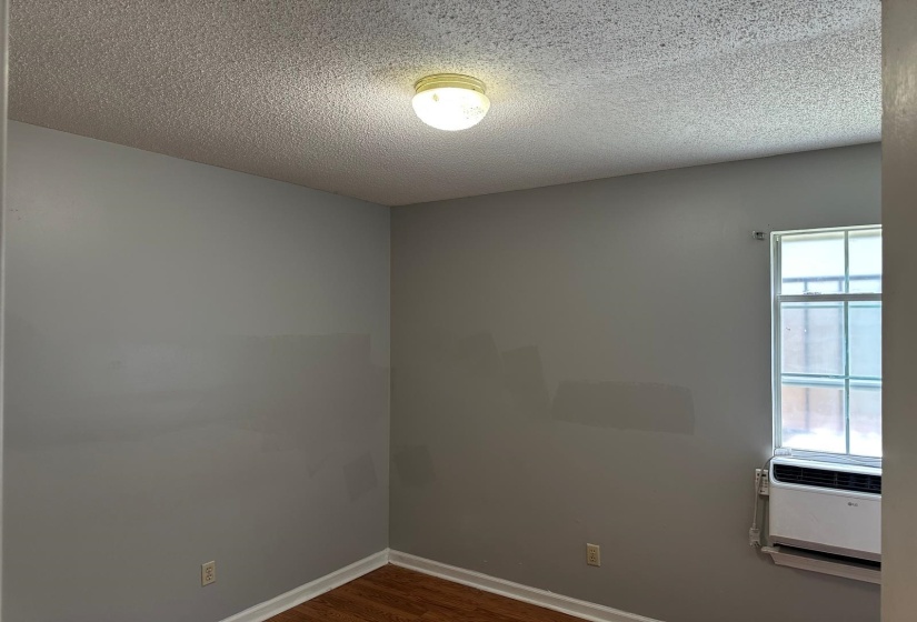 Room featuring gray painted walls, wood-finish flooring, a window-mounted air conditioning unit, and a ceiling-mounted light fixture