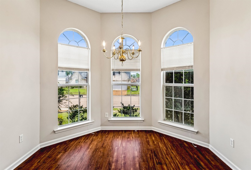 Bay window alcove featuring three arched windows with integrated blinds, a brass chandelier, wood-finish flooring, and light-toned wall paint