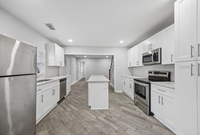 Kitchen featuring stainless steel appliances, white cabinets, wood tiled floors, a kitchen island, and recessed lighting