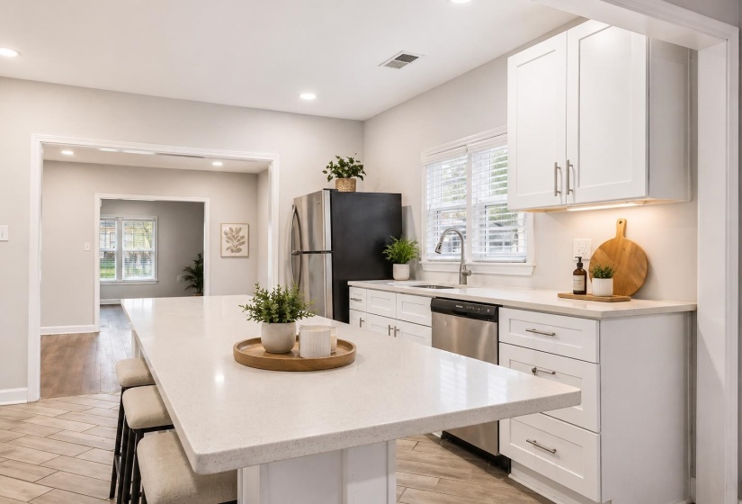Kitchen featuring a large island with seating, white shaker-style cabinetry, light-toned countertops, stainless steel appliances, and wood-finish flooring