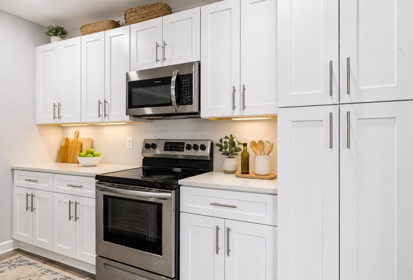 Kitchen featuring white shaker cabinetry, stainless steel appliances, light-toned countertops, and under-cabinet lighting