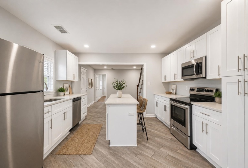 Bright kitchen featuring a central island, stainless steel appliances, white cabinetry, and light-toned wood-finish flooring