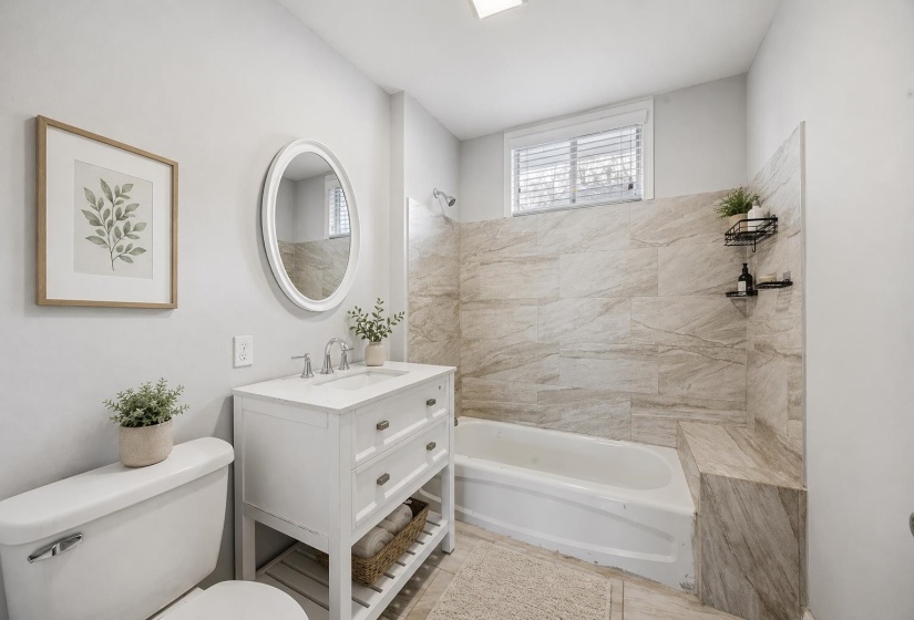 Bathroom featuring a white vanity with integrated sink, chrome faucet, oval framed mirror, and a built-in bathtub with floor-to-ceiling tile surround