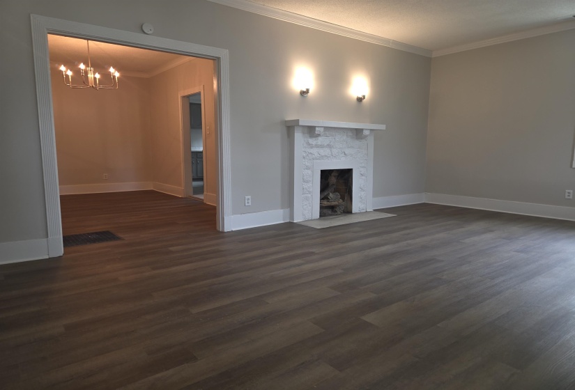 Living area featuring a white stone fireplace with sconce lighting, wood-finish flooring, light gray wall paint, and white crown molding