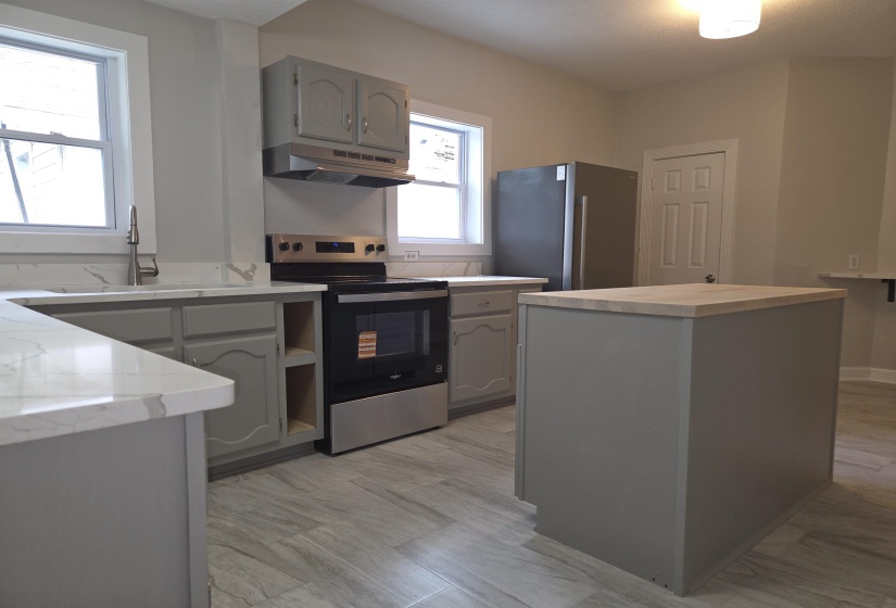 Kitchen featuring light gray cabinetry, white countertops with subtle veining, stainless steel appliances, and wood-finish flooring