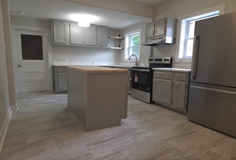 Kitchen featuring an island with a light wood-finish countertop, light gray cabinetry, stainless steel appliances, and a tile backsplash