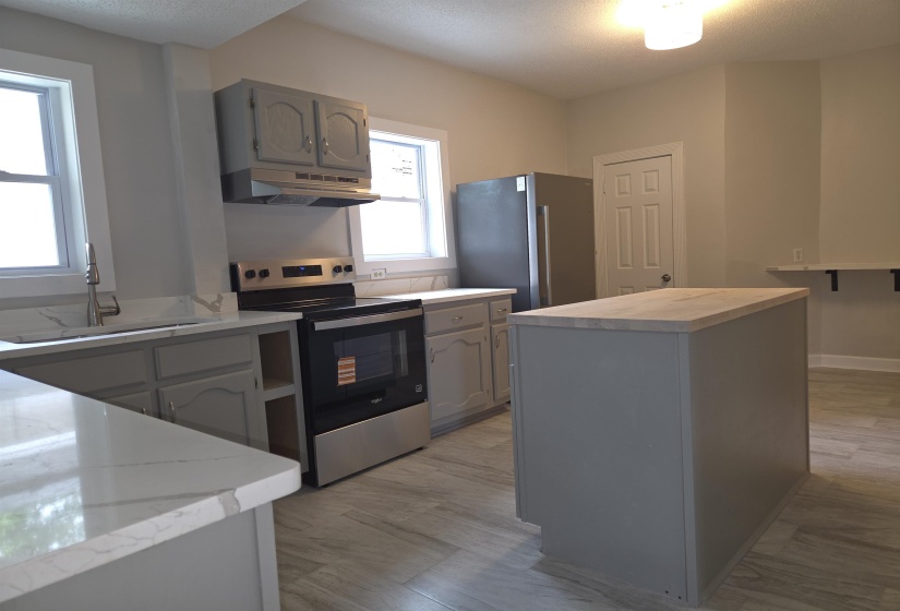 Kitchen featuring a central island with a wood-finish countertop, light gray cabinetry, stainless steel appliances, and light-toned flooring