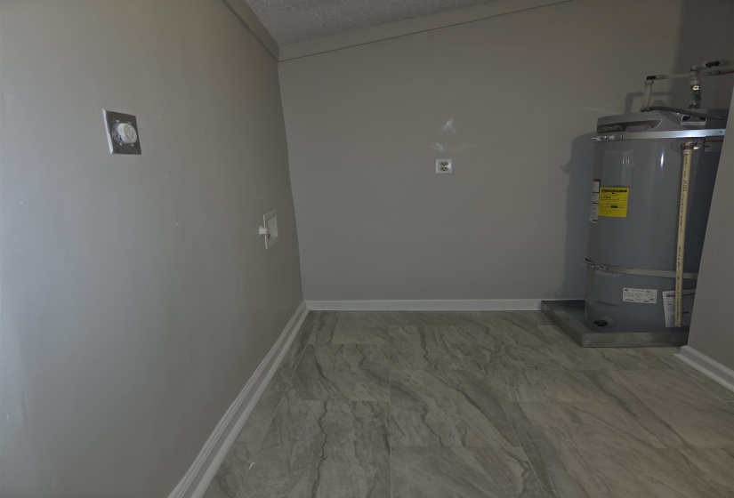 Utility area featuring a water heater, neutral gray walls, and wood-finish flooring with white baseboards