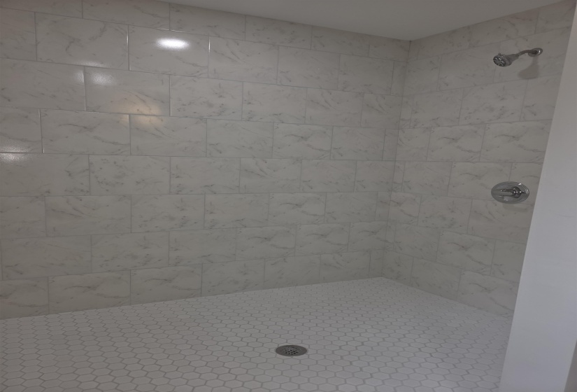 Shower enclosure with a white subway tile surround featuring subtle grey veining