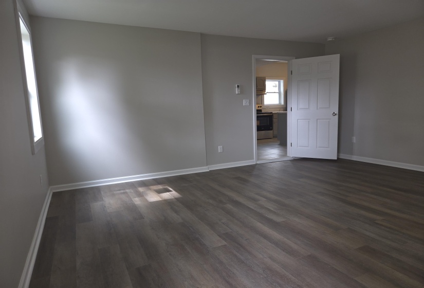 Spacious room featuring wood-finish flooring, light grey walls, white trim, and a white interior door