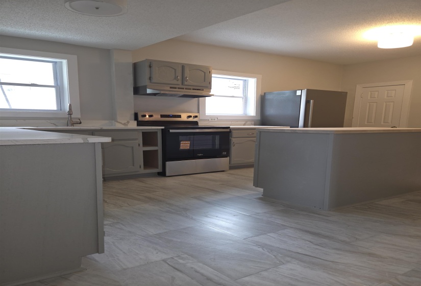 Kitchen featuring wood-finish flooring, two large windows, gray cabinetry, and a modern stainless steel appliance suite