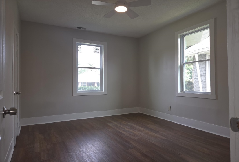 Light-filled room featuring wood-finish flooring, two double-hung windows with white trim, a ceiling fan, and painted walls