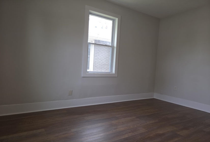 Room featuring a double-hung window with white trim, light gray walls, and wood-finish flooring