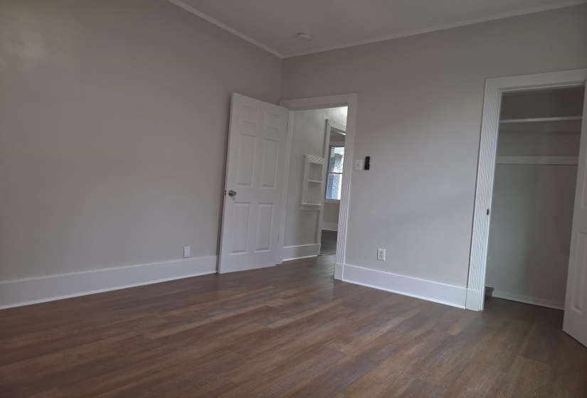 Room featuring wood-finish flooring, light grey painted walls, white trim, and a white interior door