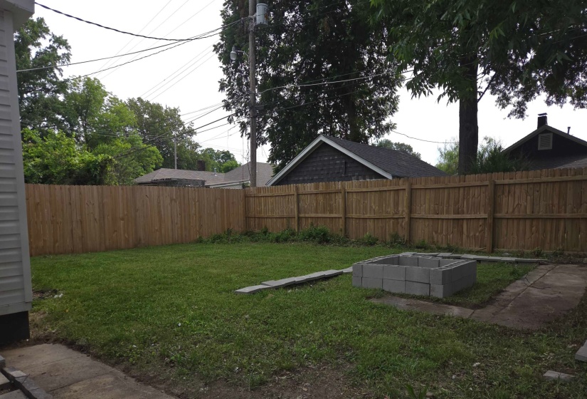 Expansive backyard featuring a new wood privacy fence, a concrete block fire pit, and established trees