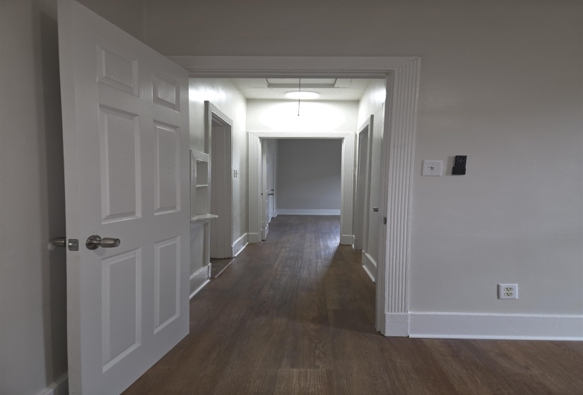 Hallway featuring wood-finish flooring, light grey painted walls, white baseboards, and a semi-flush mount ceiling fixture