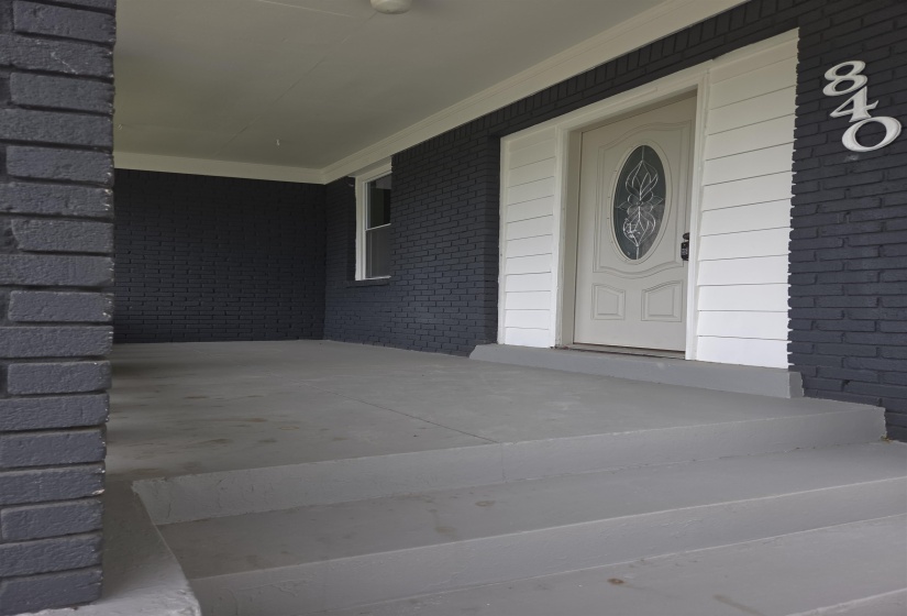 Covered porch entry featuring painted brick siding and a white paneled door with decorative glass