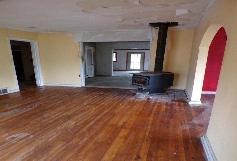 Unfurnished living room featuring a wood stove, arched walkways, and wood-type flooring
