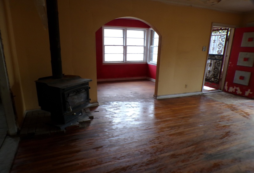 Unfurnished living room featuring a wood stove, arched walkways, and wood finished floors