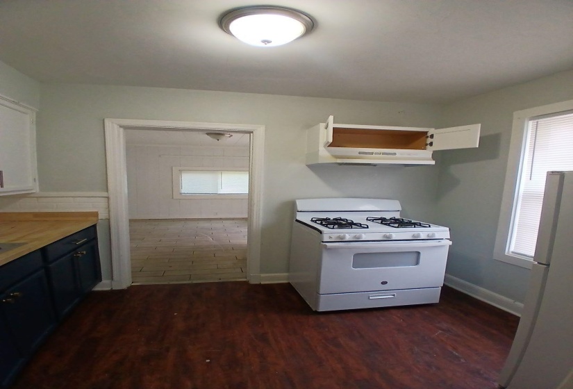 Kitchen featuring wood-finish flooring, dark blue cabinetry with light wood countertops, white gas range with overhead microwave, and recessed lighting