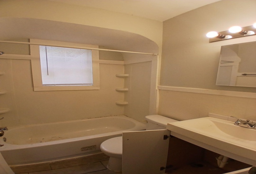 Bathroom featuring a built-in tub with shower, window with blinds, and vanity with integrated sink and storage below