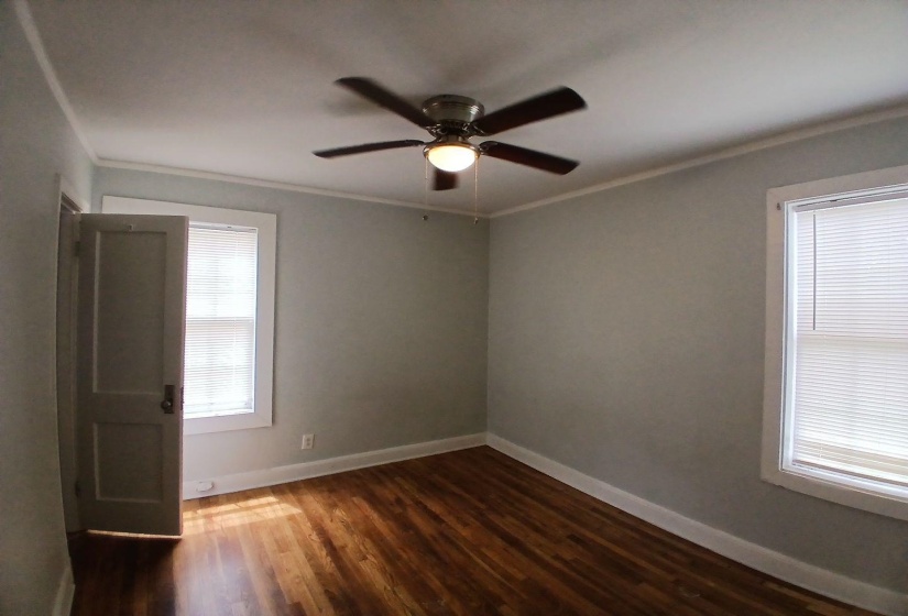 Room featuring wood-finish flooring, two windows with blinds, a ceiling fan with integrated lighting, and white baseboards