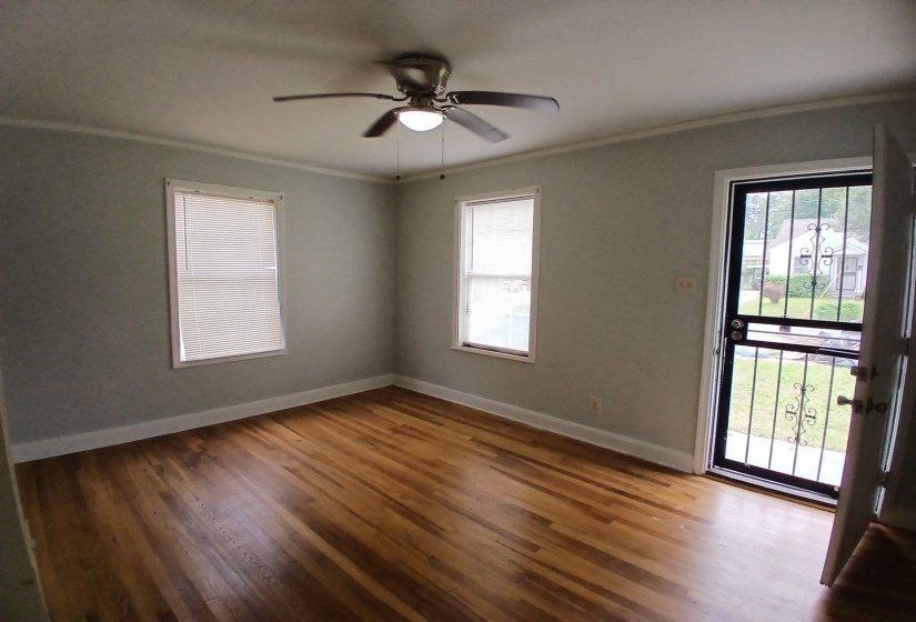 Room with wood-finish flooring, two windows with blinds, and a ceiling fan with integrated lighting