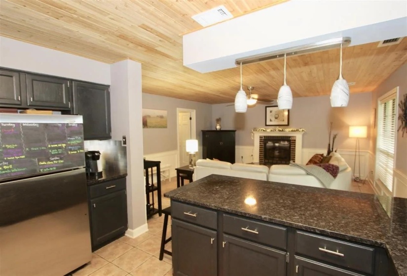 Kitchen featuring dark cabinetry, granite-style countertops, stainless steel refrigerator, and recessed lighting