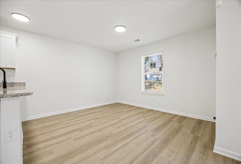 Open-concept room featuring light wood-finish flooring, recessed lighting, a single window with blinds, and white painted walls