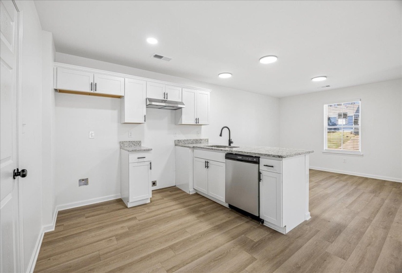 Open-concept kitchen featuring white cabinetry, light-toned countertops, and wood-finish flooring