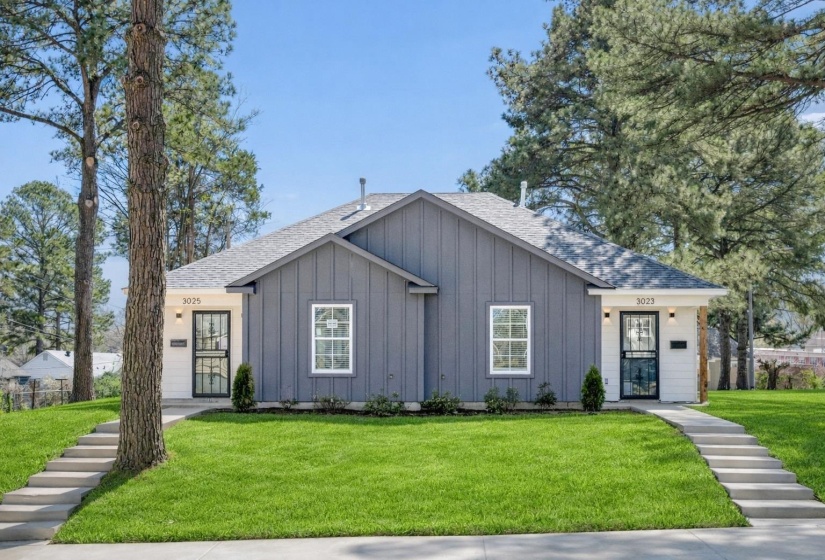 Duplex exterior featuring a gray vertical board and batten facade with white trim accents, individual concrete walkways, and dark-framed security screen doors