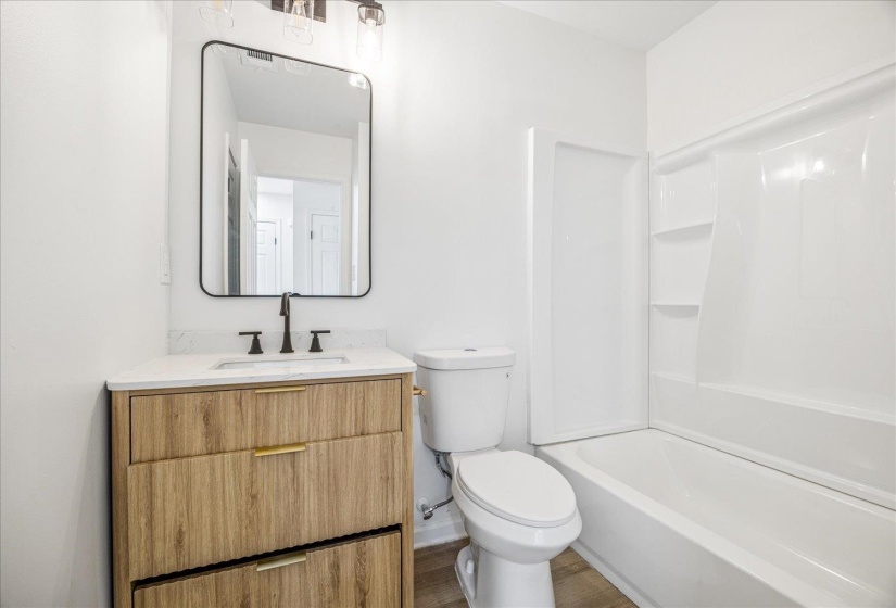 Bathroom featuring a wood-finish vanity with gold-tone hardware, a white countertop, and a black-framed rectangular mirror