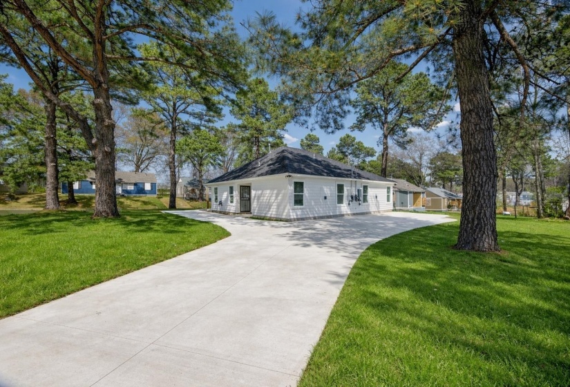 Spacious concrete driveway encircles the property, bordered by extensive green lawn