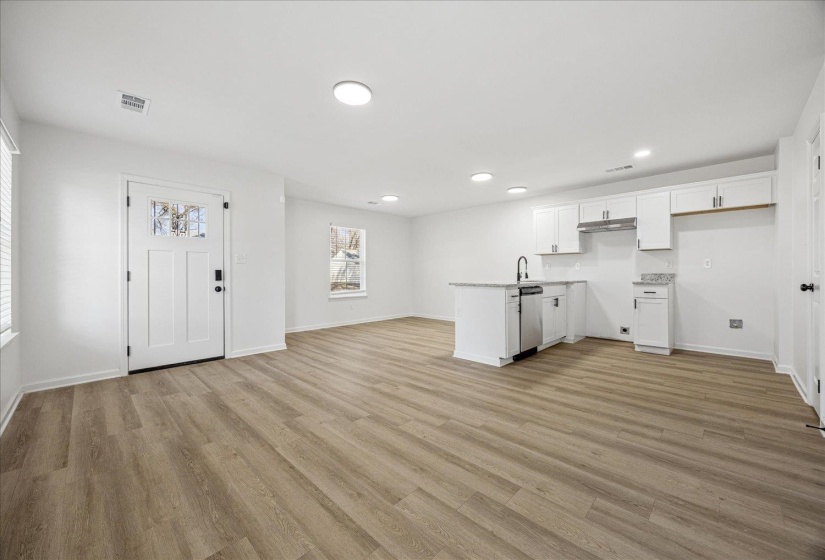Open concept living area featuring wood-finish flooring, recessed lighting, and a white kitchen with an island, stainless steel dishwasher, and a black faucet