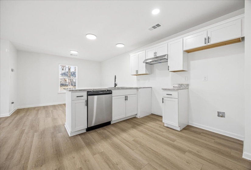 Open-concept kitchen featuring white cabinetry, light-toned countertops, stainless steel dishwasher, recessed lighting, and wood-finish flooring