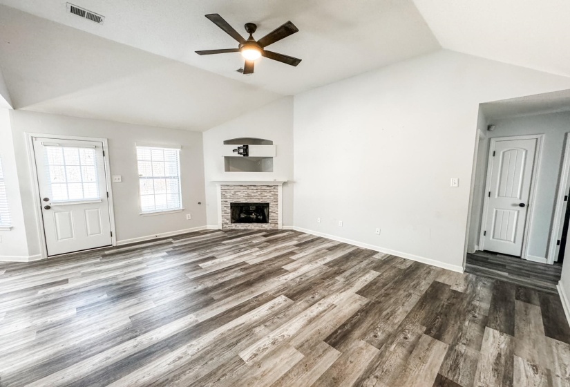 Unfurnished living room with lofted ceiling, ceiling fan, wood finished floors, and a stone fireplace