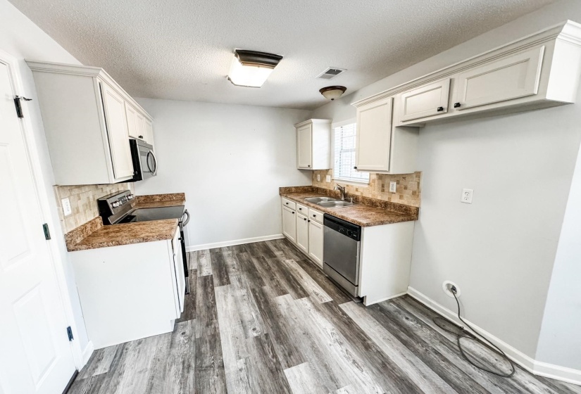 Kitchen featuring stainless steel appliances, decorative backsplash, dark wood finished floors, a textured ceiling, and white cabinetry
